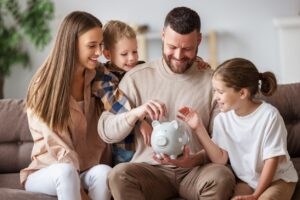A dad, mom, son, and daughter sitting on a couch and looking at a piggy bank.