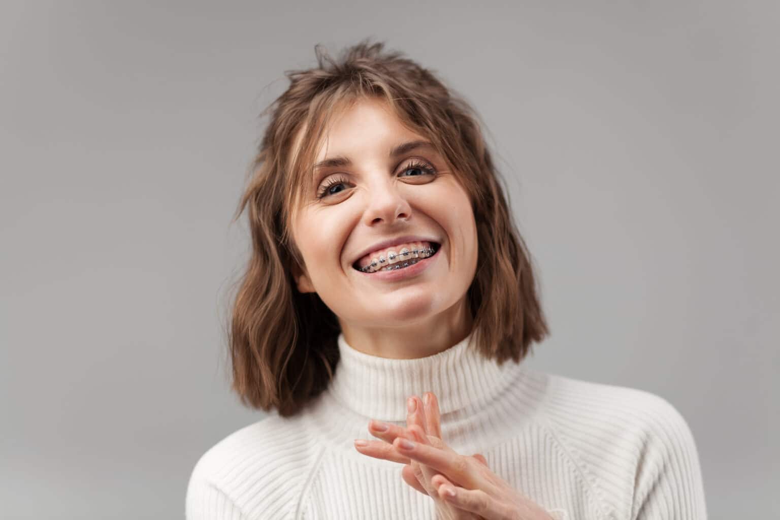 a brunette woman with a turtleneck showing off her traditional metal braces