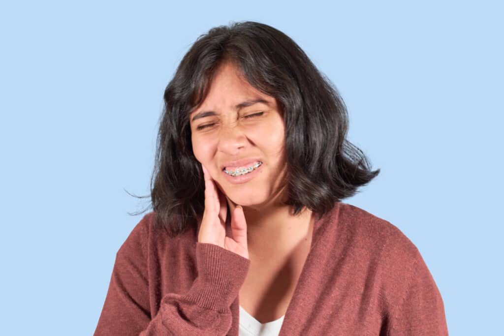 a teenage girl with orthodontic braces holding her right cheek in pain