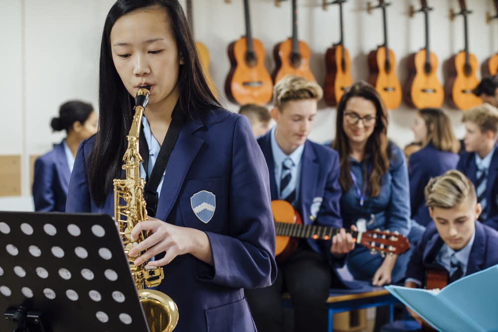 a group of teenagers in band class playing the saxophone and guitar