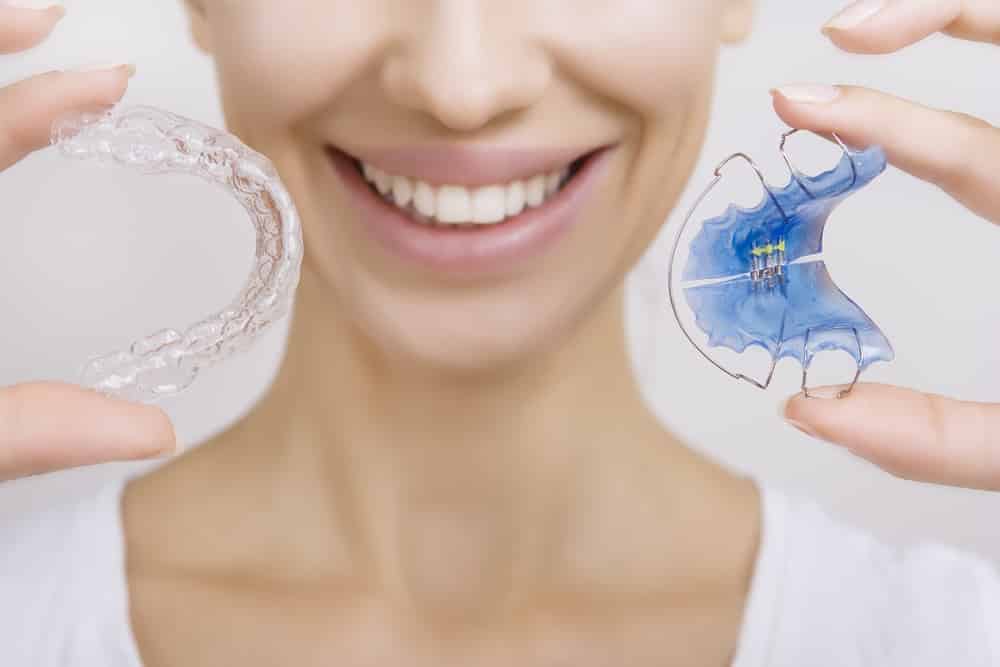 a woman showing her invisalign clear aligners and orthodontic retainer