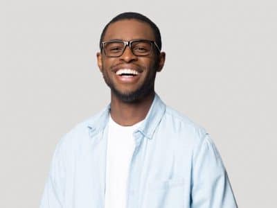 A smiling young man in eyeglasses standing in front of a grey background.